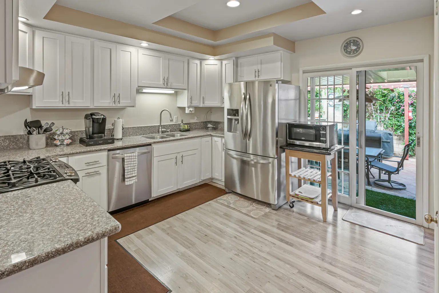 Updated kitchen with white cabinets, stone worktops and a garden view
